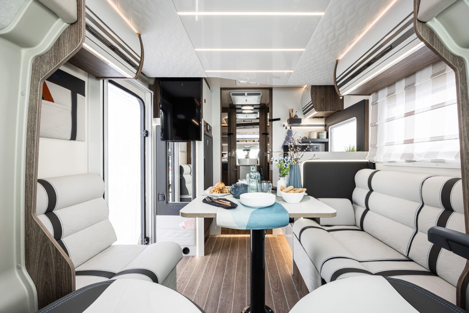 Dinette interna del camper CI con tavolo centrale, sedili imbottiti e illuminazione LED.